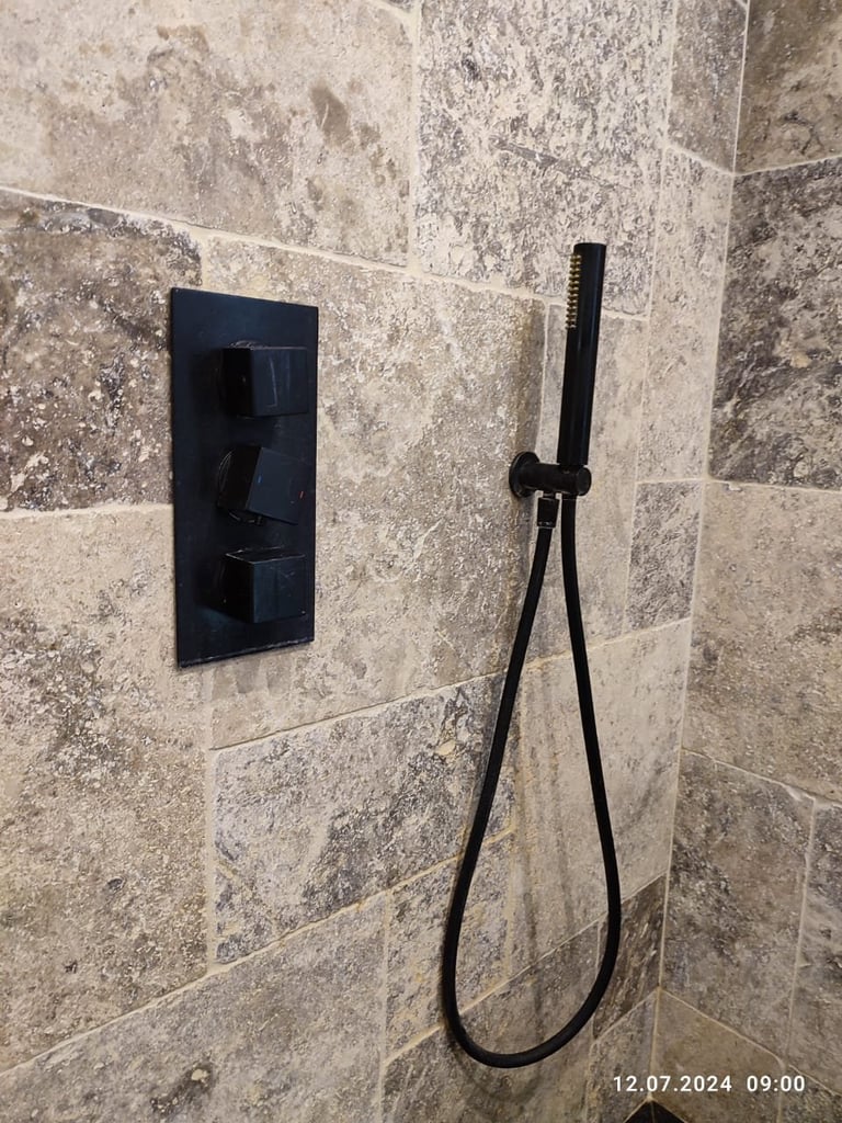 Modern black shower valve and handheld showerhead on beige travertine tile bathroom wall