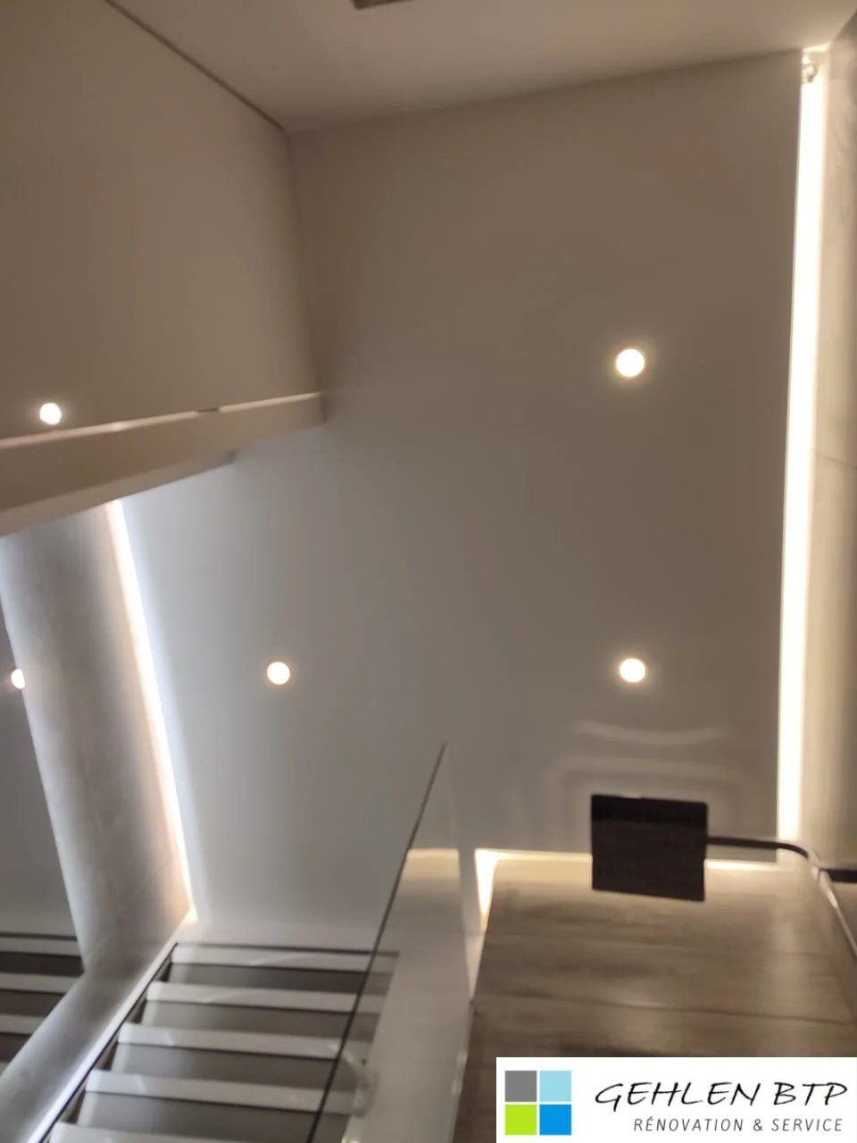 Modern minimalist stairwell with white walls, recessed LED lighting, metal handrail, and wooden steps.