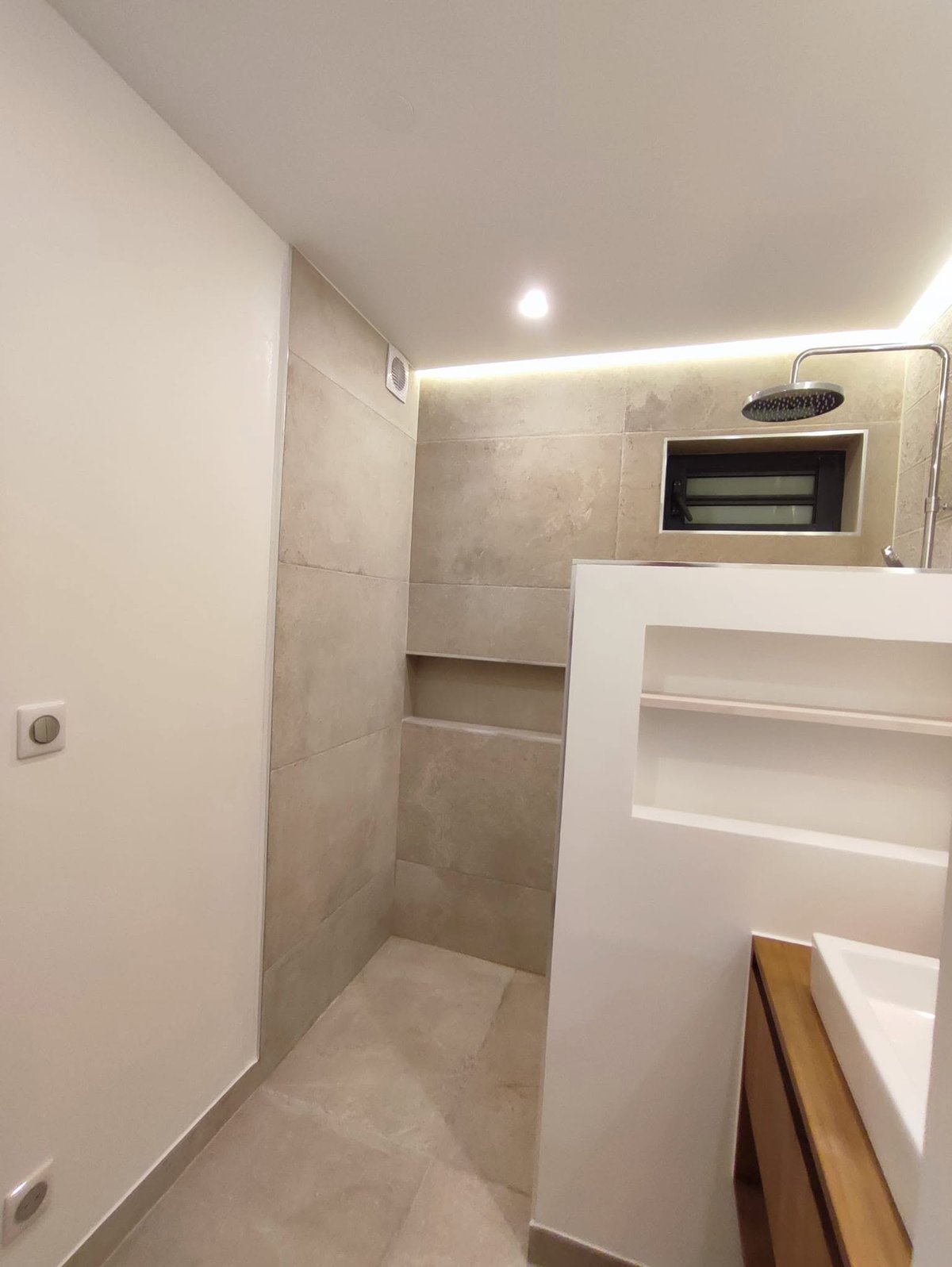 Modernes Badezimmer mit Walk-in-Dusche, beigen Fliesen, indirekter LED-Deckenbeleuchtung und weißem Waschtisch mit eingebautem Mikrowellenofen darüber
