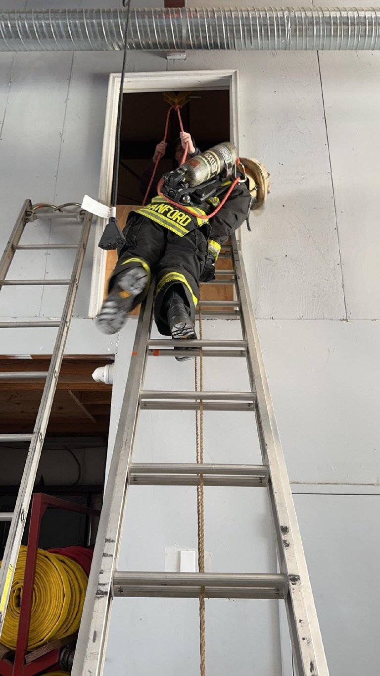 Firefighter climbing a tall ladder while carrying equipment through a building window opening
