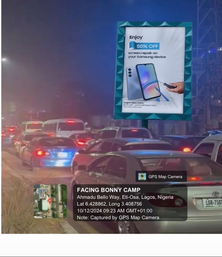 Night view of the digital billboard along Ahmadu Bello Way opposite Silverbird Galleria, Victoria Island — Samsung screen repair ad visible above queued Lagos traffic