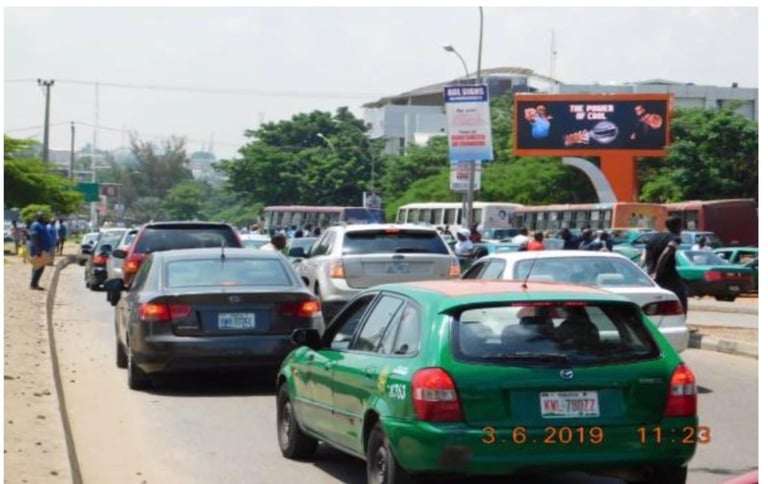 Busy urban street scene with green and blue taxis, cars, and pedestrians outside a commercial area with billboards
