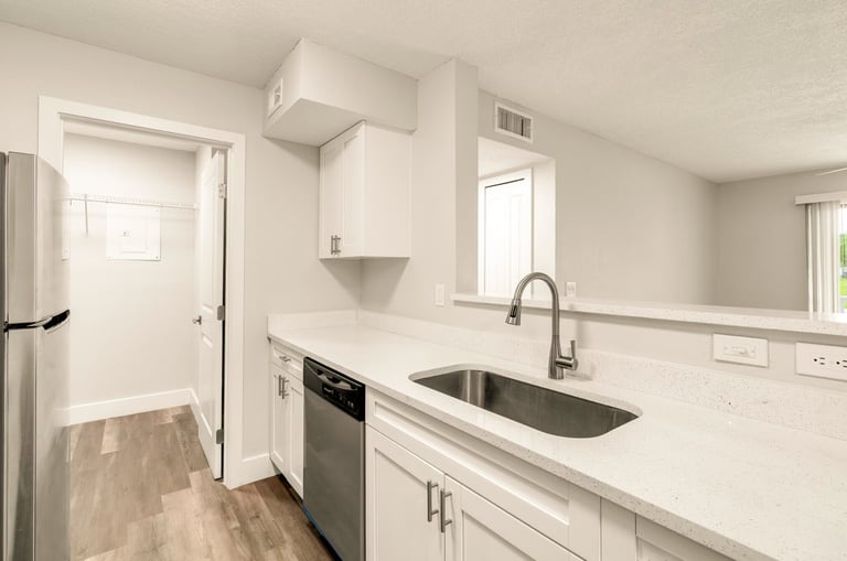 Modern white kitchen with stainless steel sink, white cabinetry, quartz countertop, and stainless steel appliances
