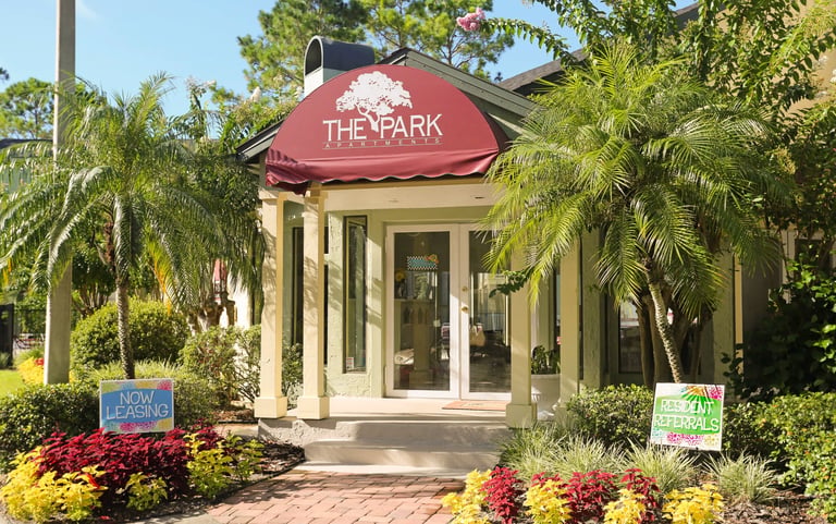 Charming cream-colored building with red awning reading The Park surrounded by palm trees and colorful landscaping