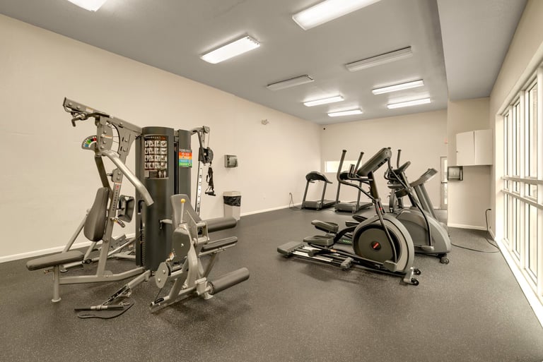 Empty modern gym interior with exercise equipment including an air bike and stationary bikes on dark flooring