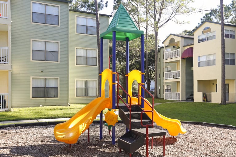 Colorful playground with yellow slides and green tower structure in residential community surrounded by apartment buildings