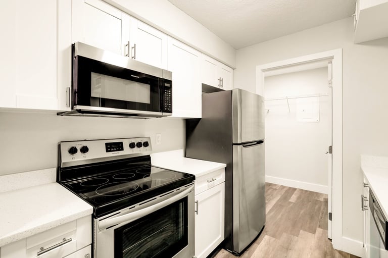 Modern kitchen with white cabinets, stainless steel appliances, and wood-look flooring