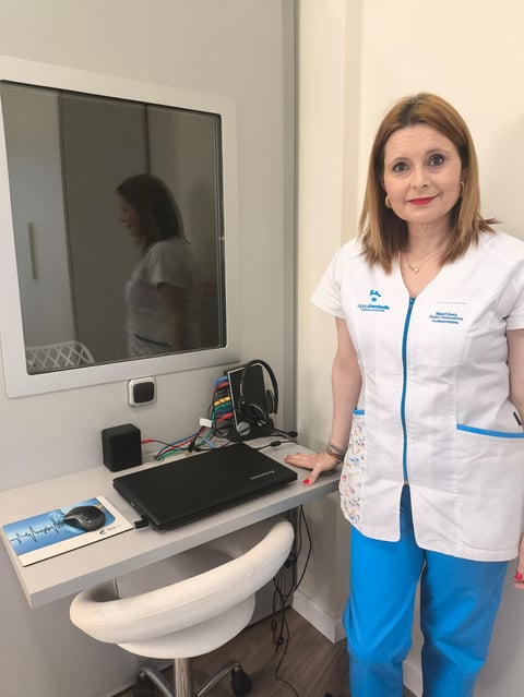 Two women in white medical uniforms stand smiling with arms crossed in front of eyeglass display wall
