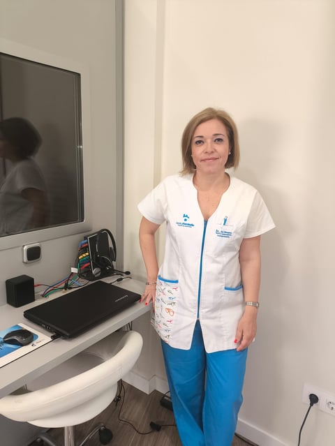 Two women in white medical uniforms stand smiling with arms crossed in front of eyeglass display wall