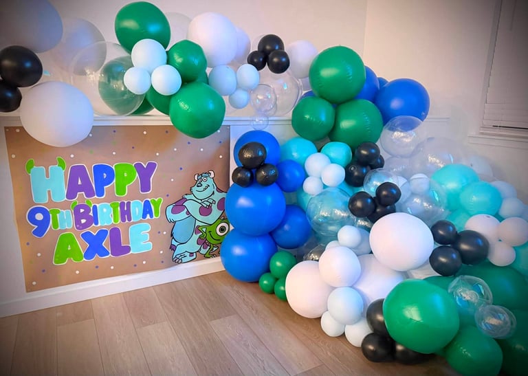 Colorful balloon arch in green, blue, white, and black with Happy 9th Birthday Axle sign on kraft paper backdrop