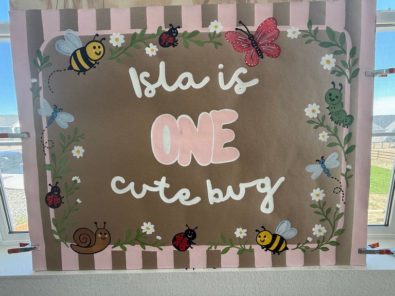 First birthday sign for Isla featuring cute bug decorations, white text on brown background with pink striped border