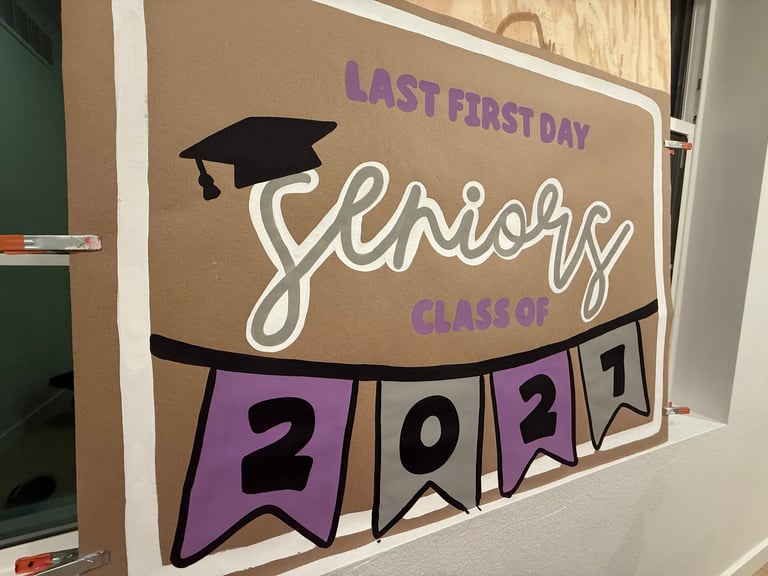 Bulletin board display reading Last First Day Senior Class of 2027 with graduation cap and purple pennant banner with date numbers