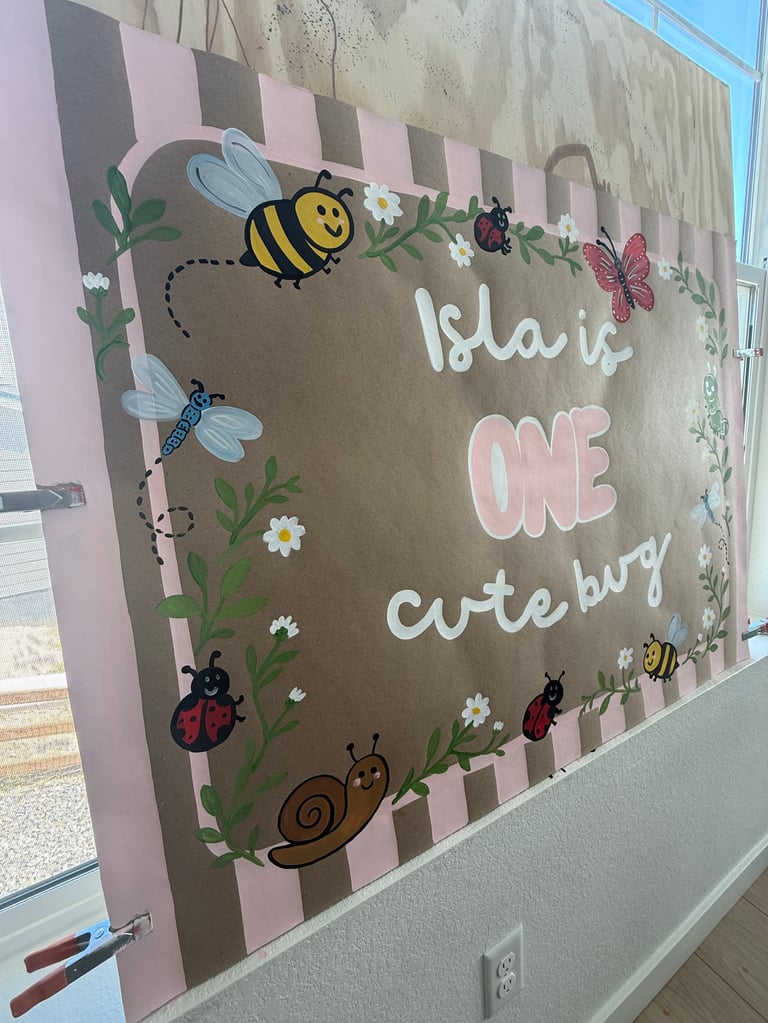Baby's first birthday wall decoration with cute bugs, flowers, and text saying Isla is ONE cute bug on a striped background