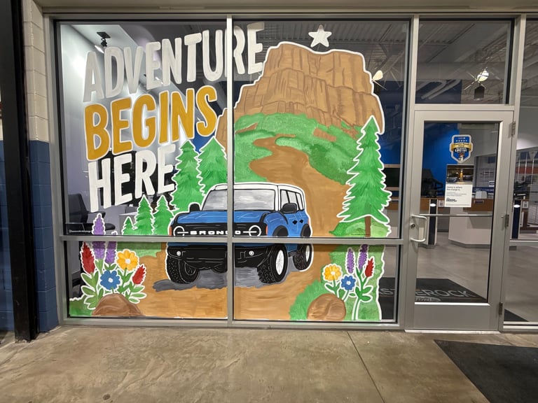 Adventure themed window display with off-road truck, mountains, trees, and text reading Adventure Begins Here