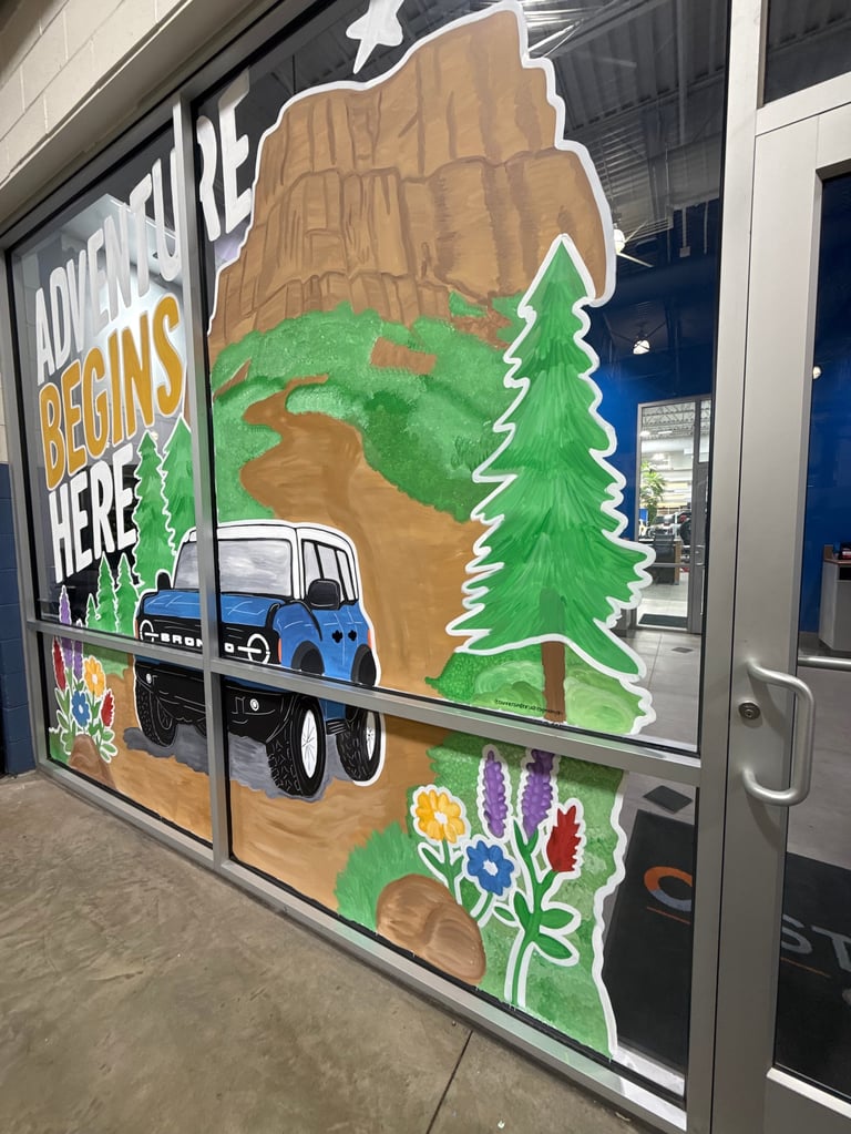 Large mural on storefront window featuring colorful illustrated Maine landscape with blue truck, evergreen tree, mountains, and wildflowers