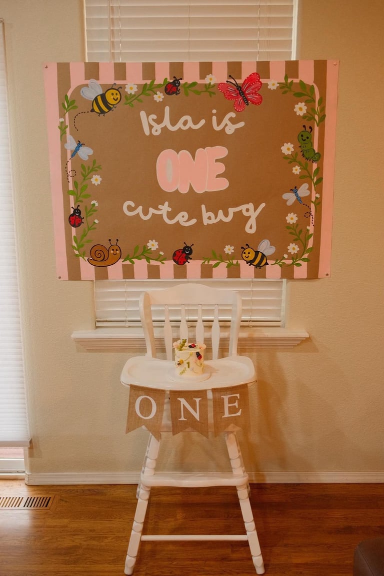 First birthday decoration setup with sign reading Isla is ONE cutebug above white high chair with ONE banner