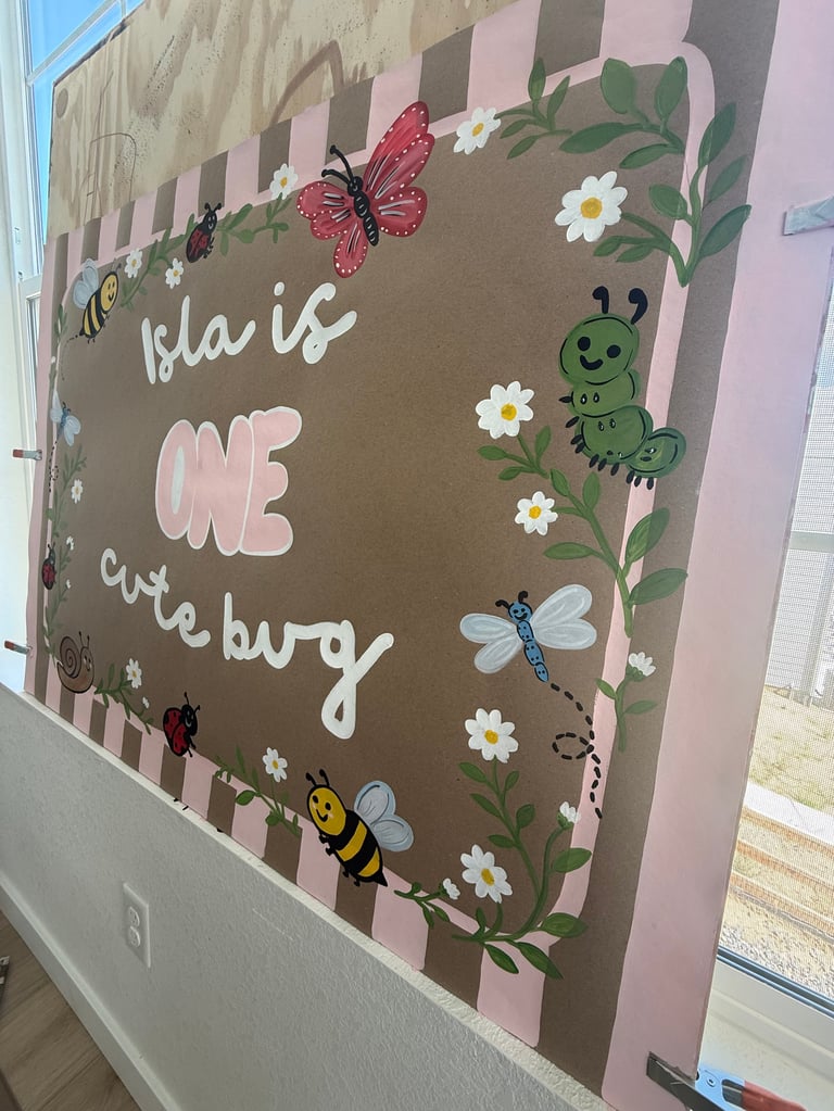 Wall sign with She is ONE cute bug text decorated with colorful insects, flowers, leaves, and a checkered border in pink and brown