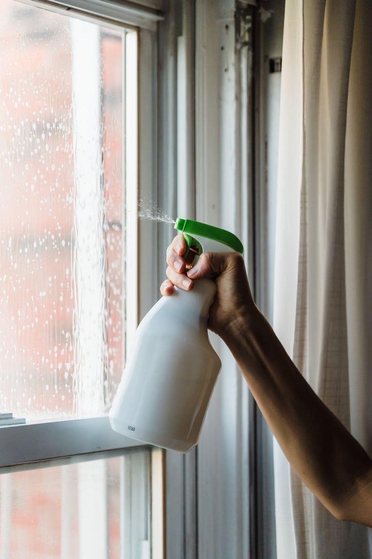 Hand spraying window cleaner on a wet window with a spray bottle