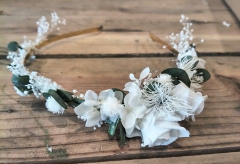 White floral bridal crown with delicate flowers and greenery on wooden surface