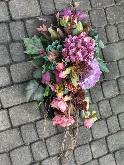 Floral memorial arrangement with purple hydrangeas, pink roses, and greenery laid on a brick surface