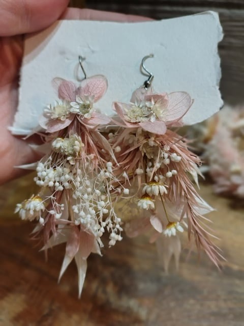 Pair of hanging earrings made with dried pink flowers and white babys breath on metal hooks, held in hand