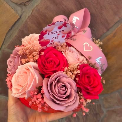 Hand holding a bouquet of pink and red roses with babys breath and pink decorative tags on wooden background