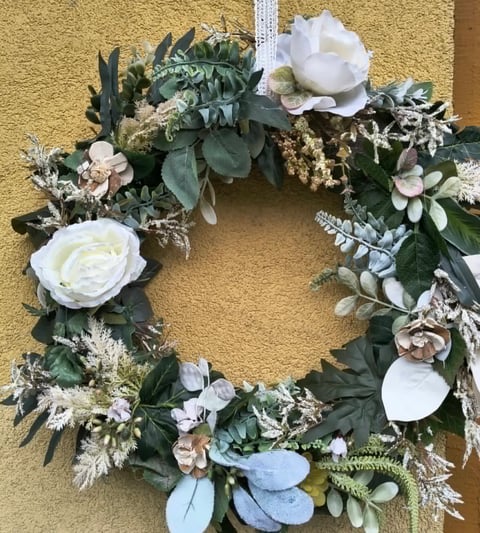 Decorative wreath with white roses, eucalyptus, dusty blue flowers, and dried foliage on textured yellow wall