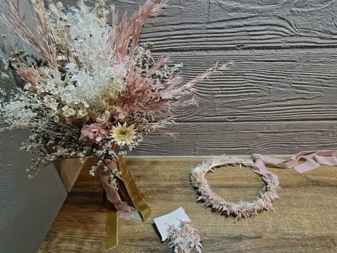 Dried flower arrangement in vase with wreath and corsage on wooden surface against gray wooden backdrop