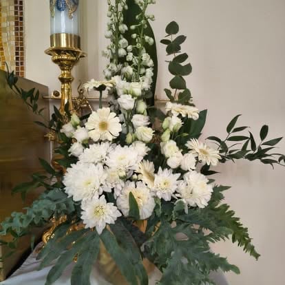 Elegant floral arrangement with white daisies and greenery in a decorative vase next to a gold candle holder