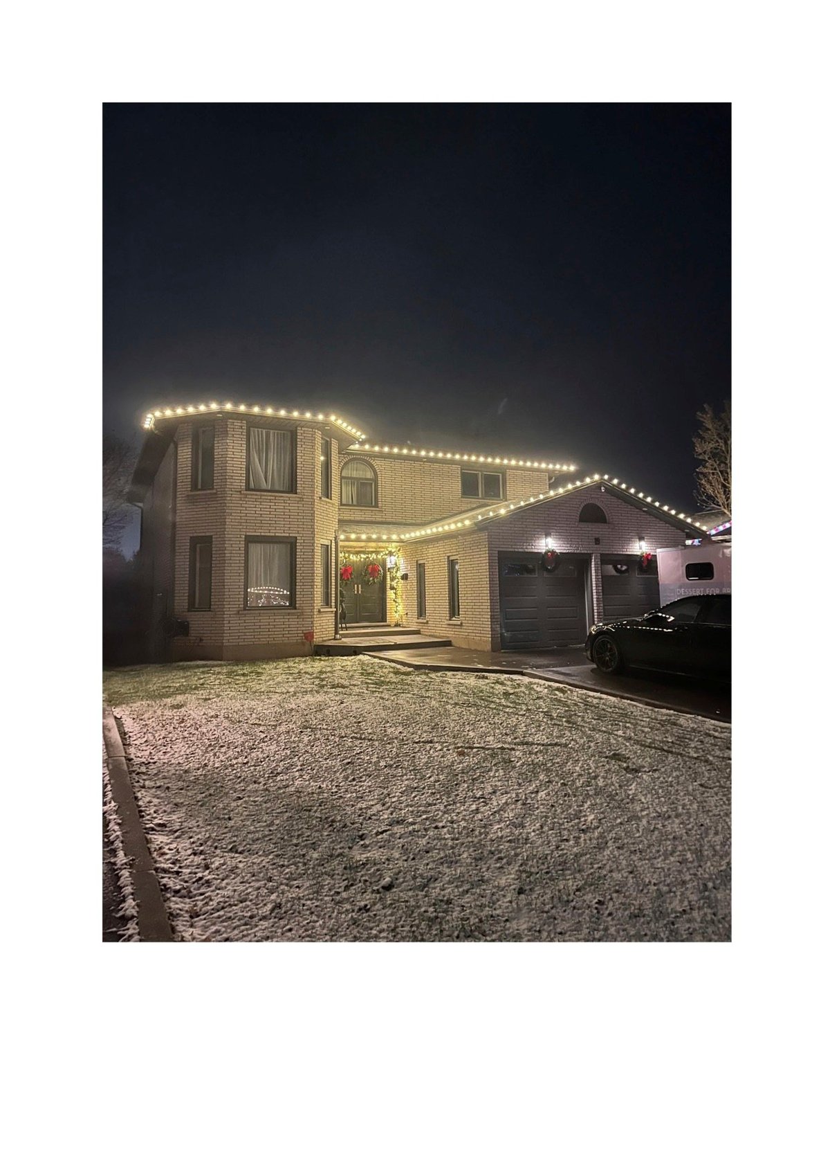 Brick two-story house decorated with warm white string lights at night, featuring a driveway and garage