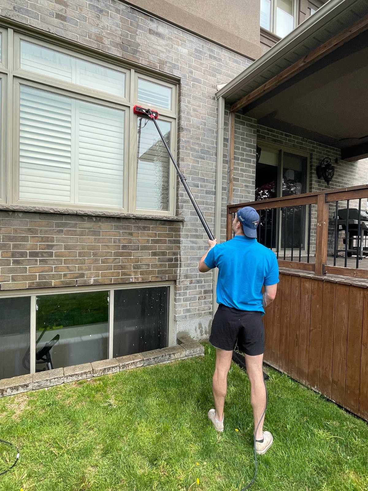 Man in blue shirt jogging on grass with telescoping pole near brick house with windows