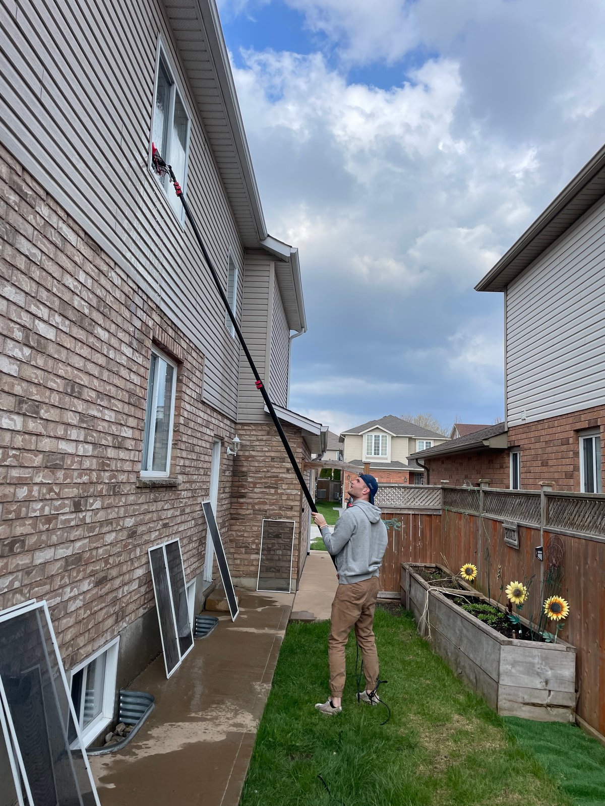 Man cleaning brick house exterior with pressure washer wand in residential backyard