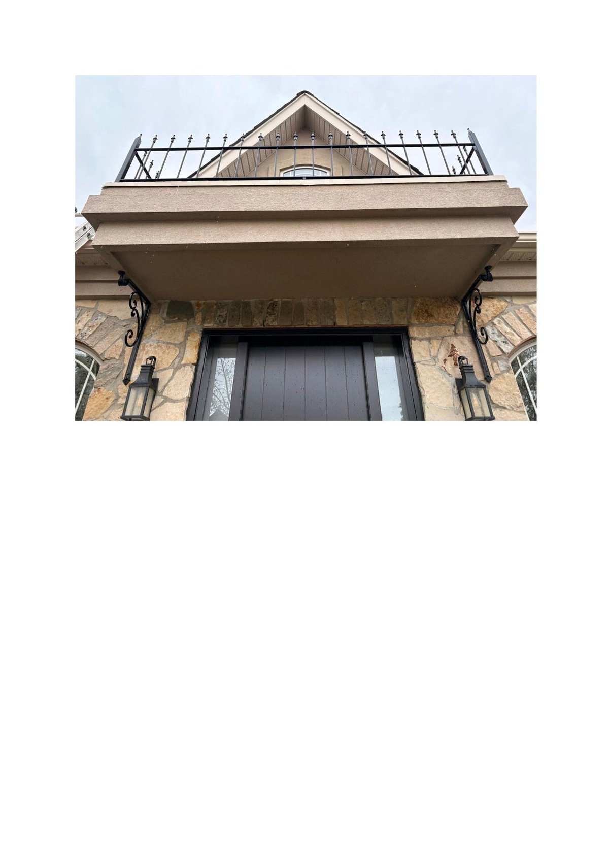 Stone building roofline with decorative metal railing, peaked dormers, and dark wooden entrance door with wall sconces