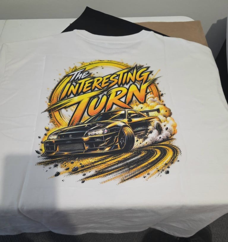 White t-shirt with yellow and black graphic design featuring a race car and The Interesting Turn text