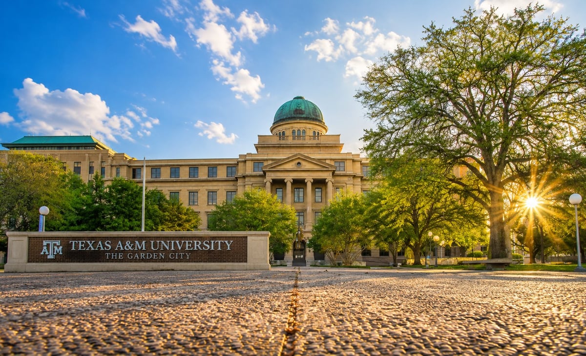 Texas A&M University historic campus building with green dome, stone courtyard, and tree-lined grounds under blue sky. Independent campus housing information for Texas A&M University.