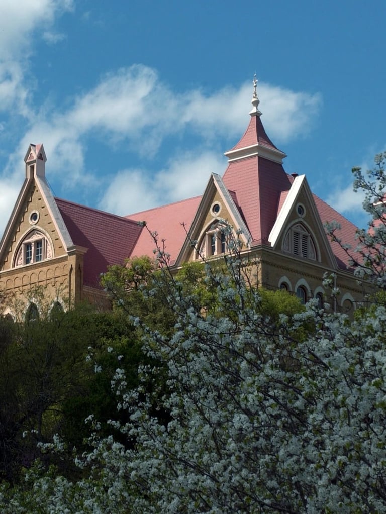 Old Main at Texas State University in San Marcos, Texas — historic Victorian building with red pitched roofs and a central spire under a clear blue sky. Independent campus housing information for Texas State University.