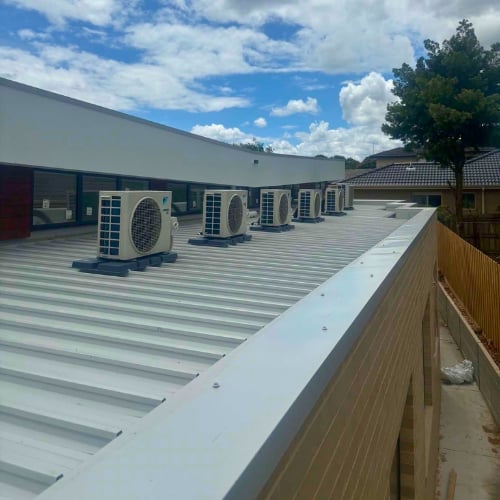 Industrial rooftop with multiple HVAC air conditioning units installed on corrugated metal roof under blue sky