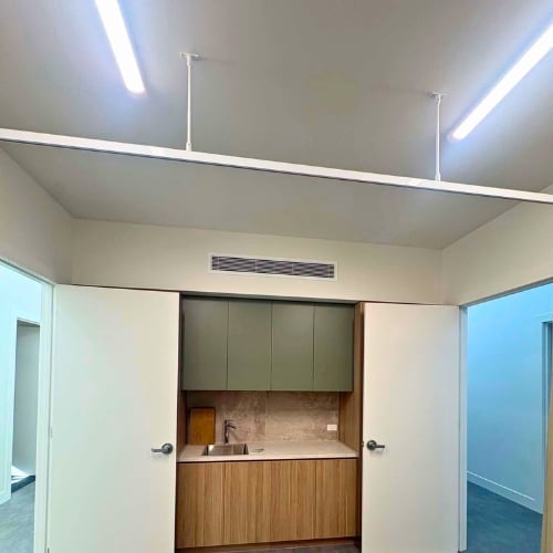 Modern interior hallway with beige walls, LED ceiling lights, and a wood-trimmed kitchenette with olive cabinetry