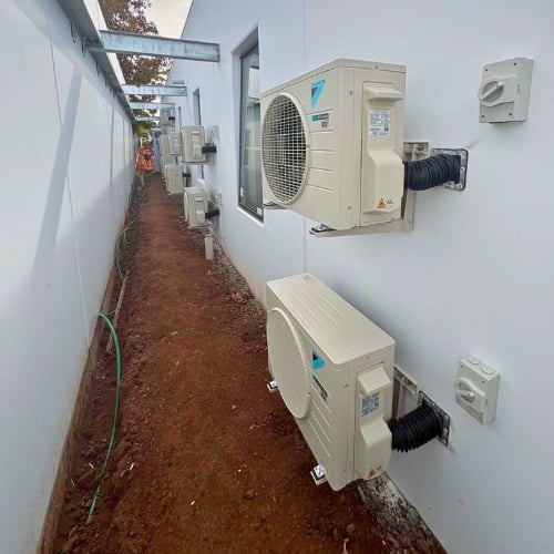 Outdoor HVAC units mounted on white wall of narrow alley with brown ground