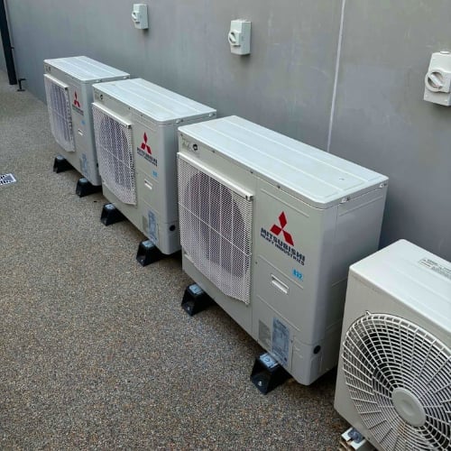 Row of Mitsubishi air conditioning outdoor units lined up against a gray wall in an indoor facility.