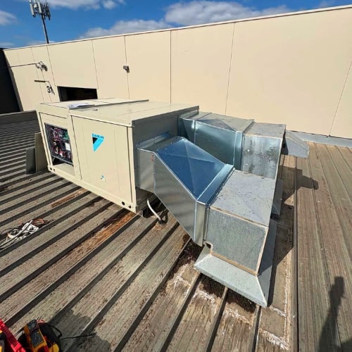 Rooftop HVAC unit with blue ductwork and metal components on wooden deck next to beige building exterior
