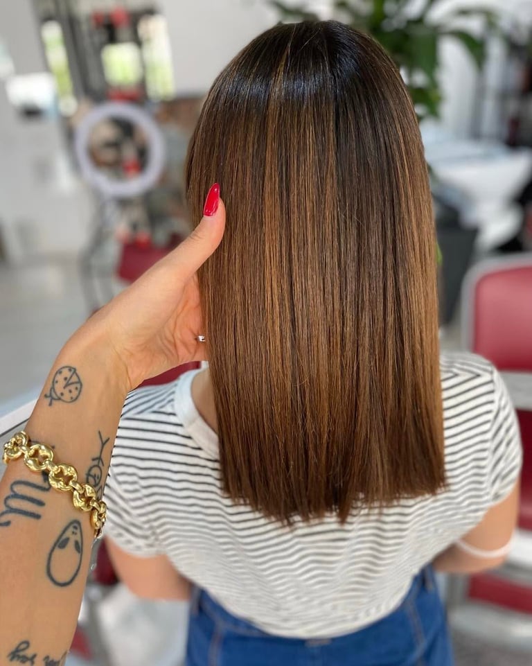 Woman with long straight brown hair and red nails in a salon, showing off sleek hairstyle from behind