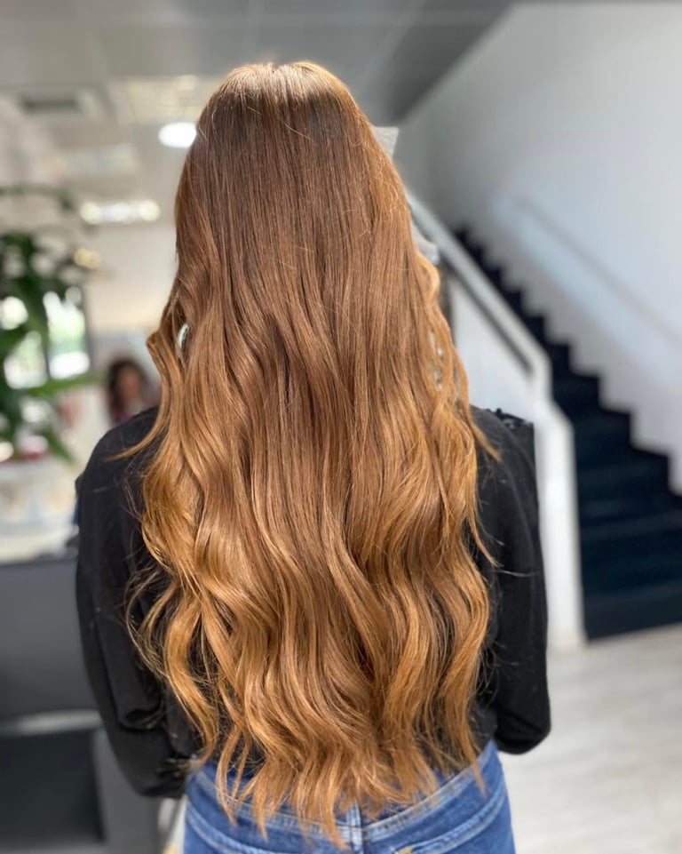 Woman with long wavy caramel brown hair wearing a black top, photographed from behind in an indoor setting