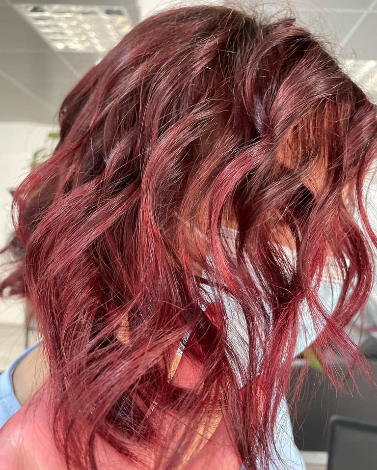 Woman with layered burgundy and rose-tinted hair with wavy texture, shown from behind in indoor lighting