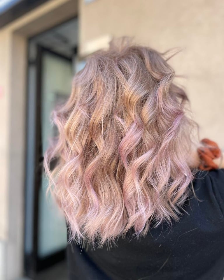 Person with long wavy blonde and pink ombre hair styled with loose waves, shown from behind against a beige wall