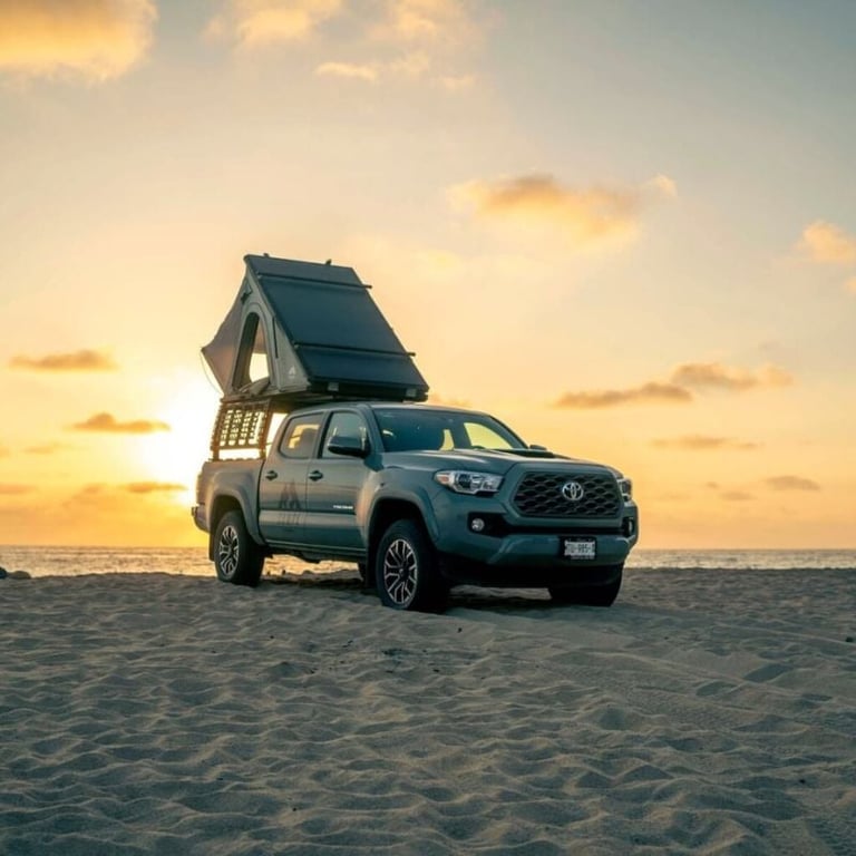 Blue pickup truck with pop-up roof tent parked on beach at sunset