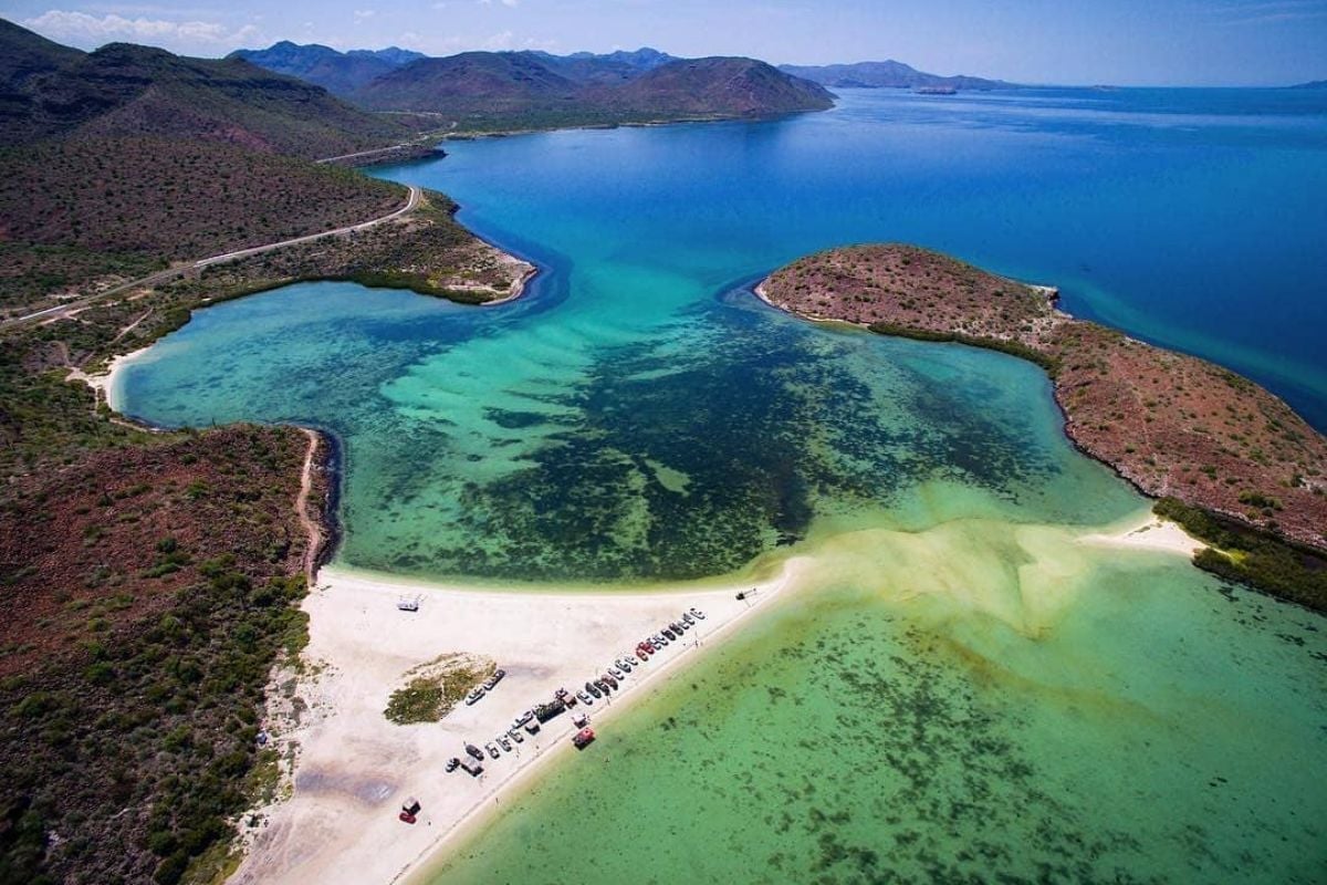 Vista aérea de una playa virgen con aguas turquesas, arena blanca e islas rocosas boscosas en Baja California Sur