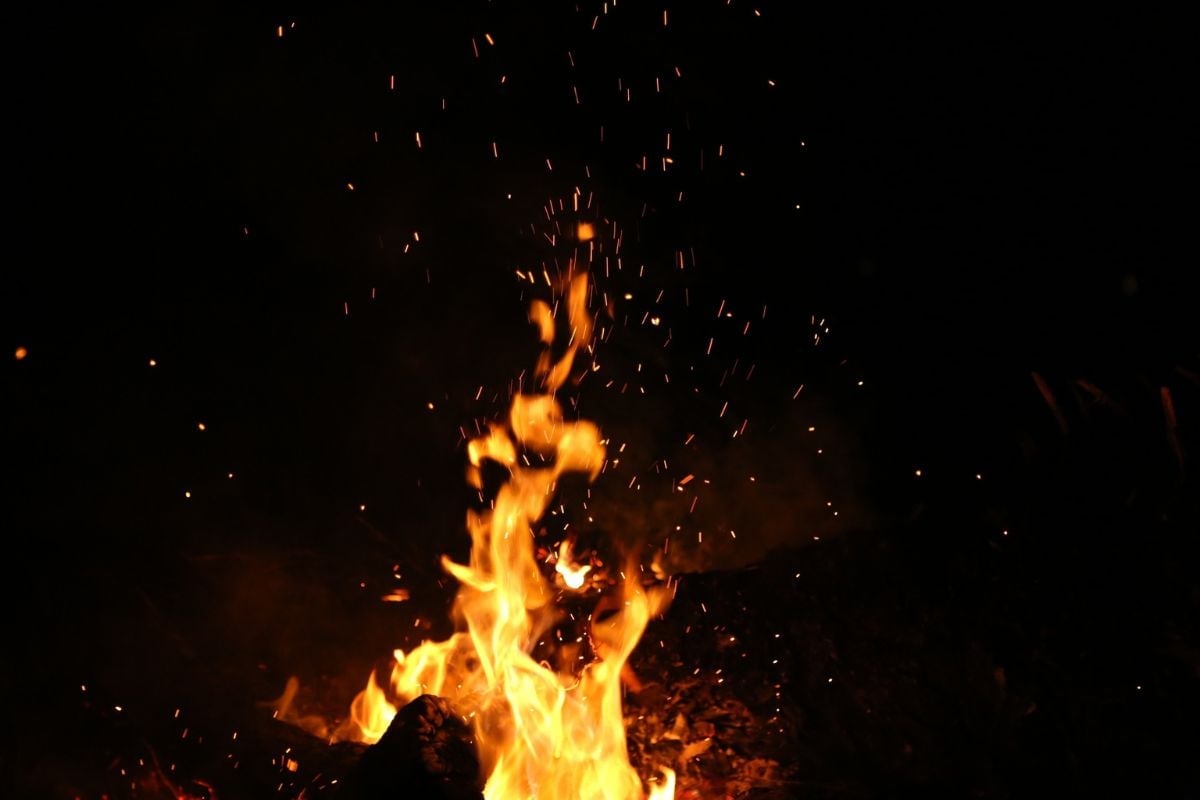 Bright orange and yellow flames rising from a campfire against a dark background with glowing embers and sparks
