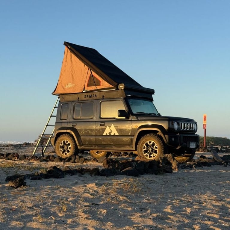 Rugged jeep with orange pop-up tent parked on a beach at sunset, equipped for adventure travel