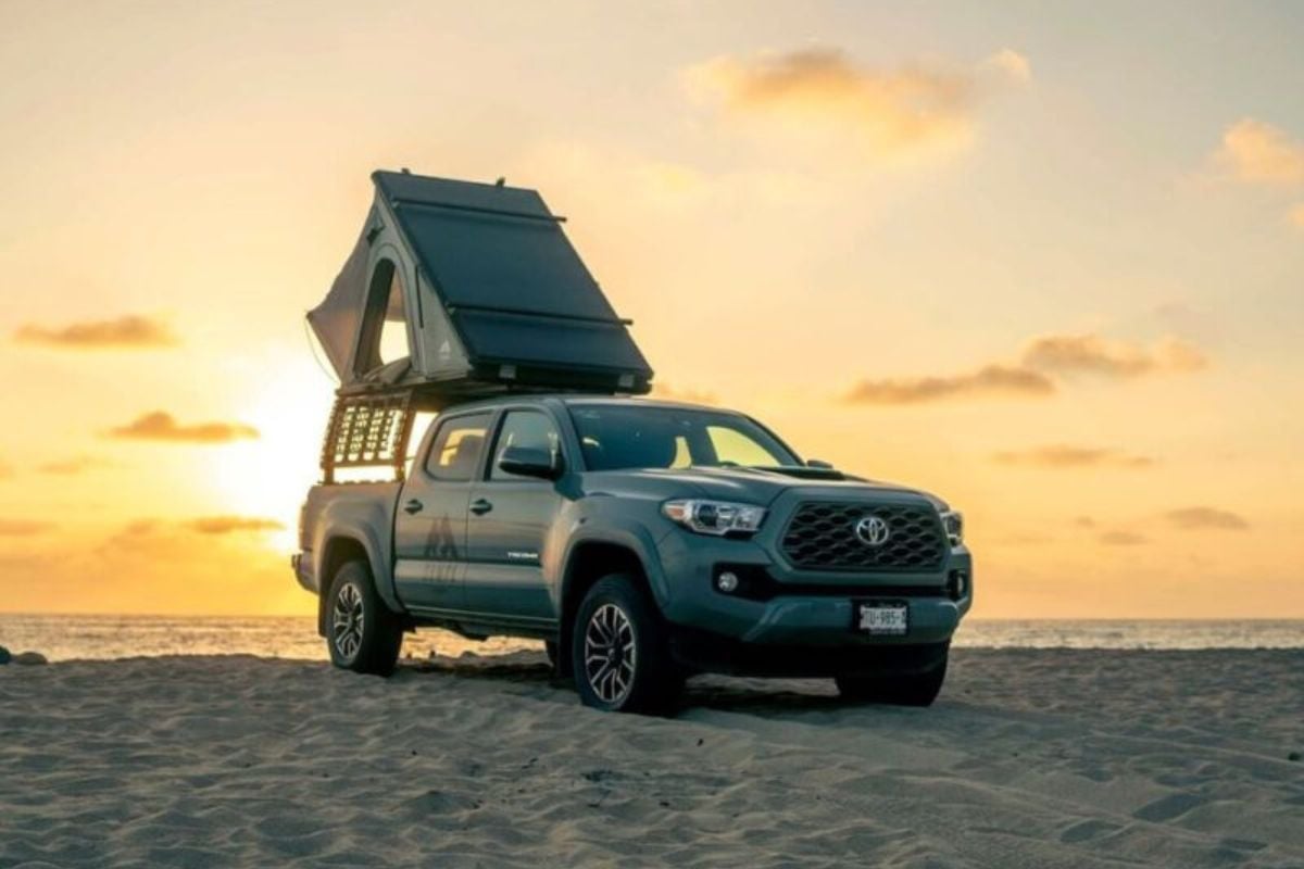 Blue Toyota pickup truck with pop-up camper on sandy beach at sunset